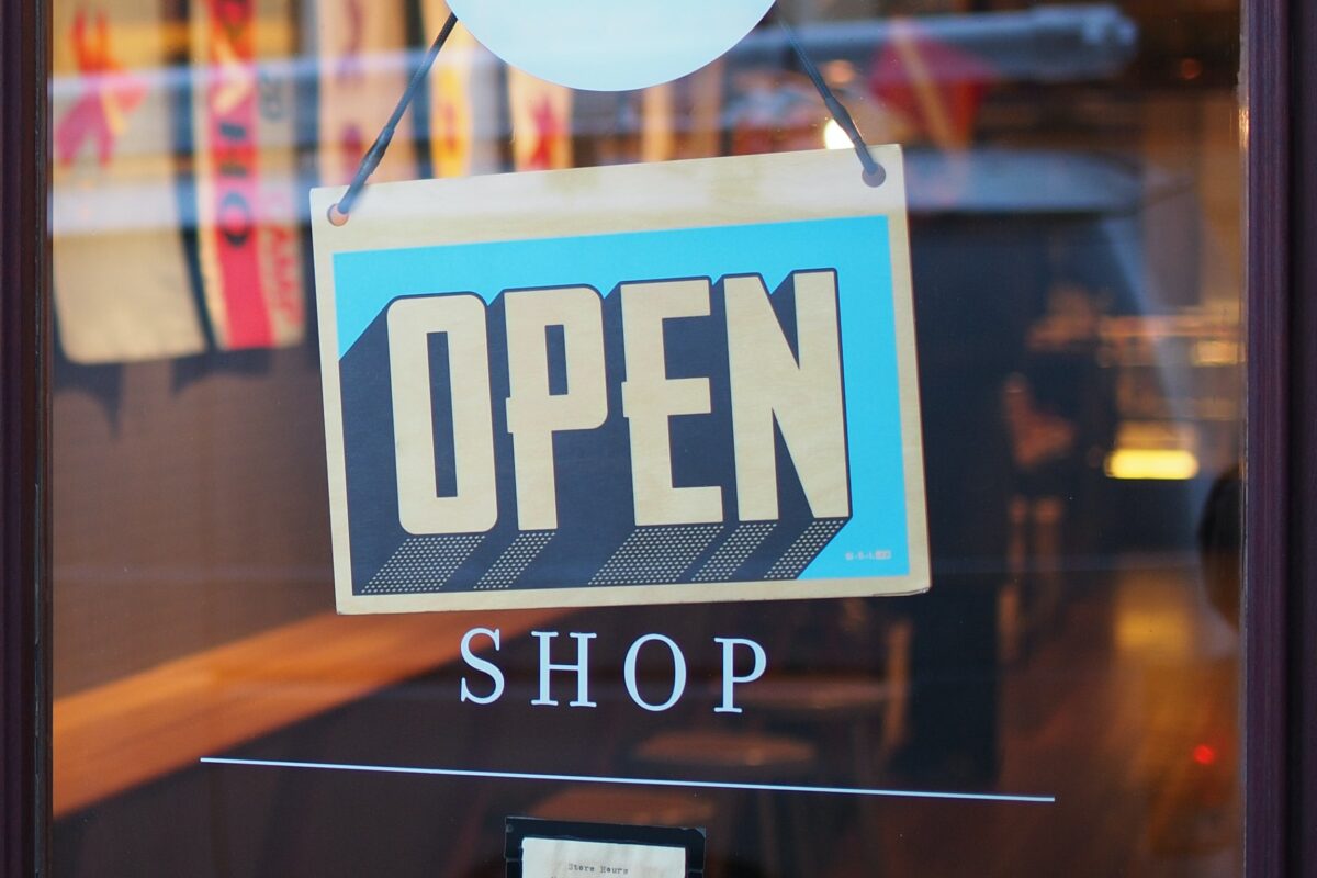 deals for small businesses: a glass shop door with a black and blue "Open" sign hanging from it.