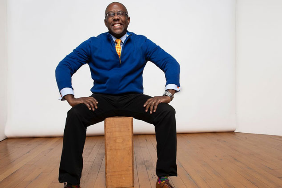 entreprenuer-in-residence Ramon Ray sits with hands on legs, blue sweater, black pants, yellow tie, smiling