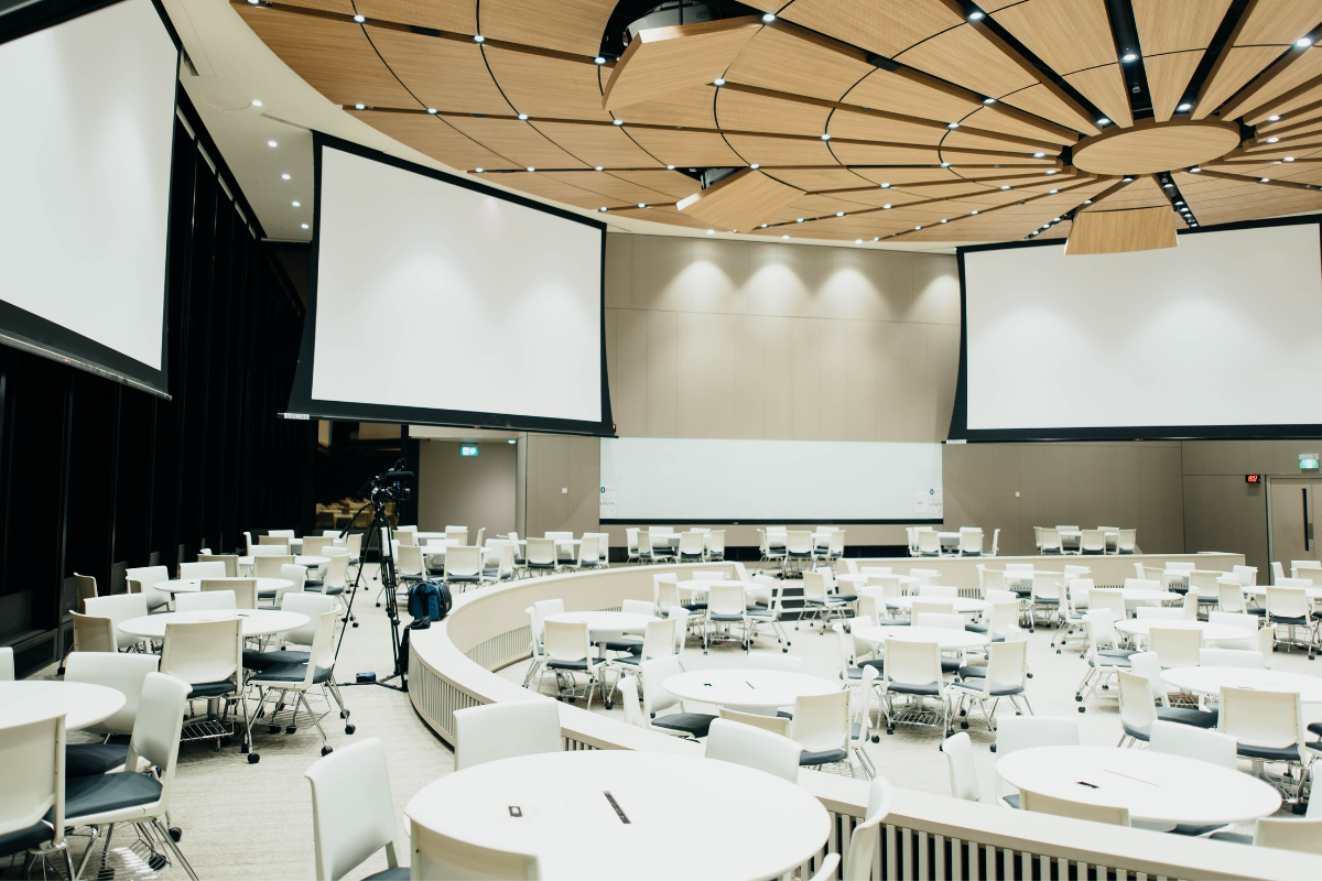 Pitching for Profit: Empty room with white tables, chairs, and screens prepared for a speaker